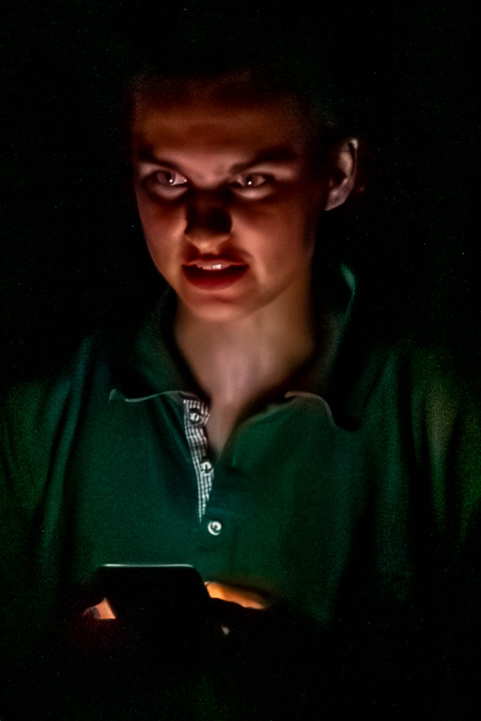 Artistin spricht und wird von unten von dem Handybildschirm beleuchtet, der Raum ist dunkel.